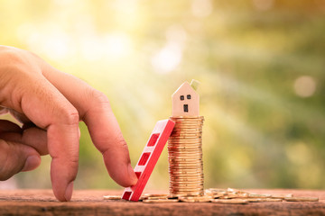 Close up of hand with climb up on  red steps and stacking gold coin with growing and home model as destinations on sunlight background, Loan for real estate or buy a new house in the future concept.