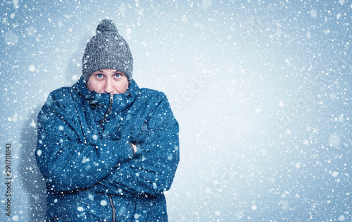 Cuadros en Lienzo Frozen man in a blue jacket and hat stands against the wall, snow is falling aro