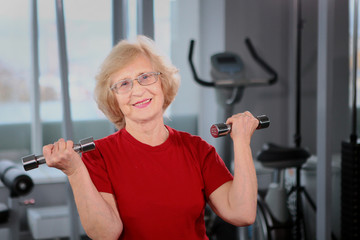 An elderly woman holds dumbbells in her hands. Active retirement lifestyle concept.