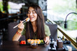 © F8  \ Suport Ukraine - Young woman eating and enjoying fresh sushi in luxury restaurant. Female client holding food sticks and eating oriental meal on lunch. Concept of food.