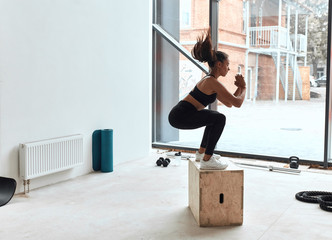 Wall Mural - Box jumping at crossfit style in gym, box jump performing of young fit girl. Window background