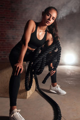 Wall Mural - Young fit girl take rest after training in gym, looking at camera. Working out with ropes in gym. Brickwall background