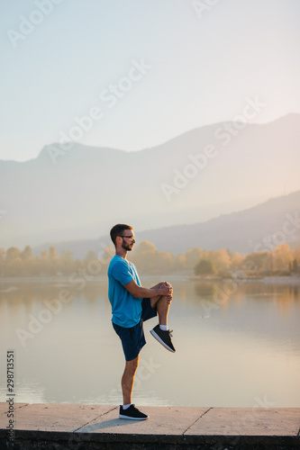 Fotografía Young man in sportswear stretching by the lake in a city park