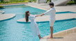 © May Chanikran - Happy young couple holding each other and walking by the swimming pool with happiness together, close up, romantic couple spending time concept.