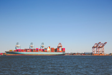 Landscape orientation of Freighter ship docked with cargo with cranes unloading cargo.