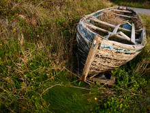 Old Rustic Wooden Fishing Boat Ashore In The Grass, Damaged Beyond Repair