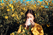 © Volodymyr - Pollen allergy concept. Young woman is going to sneeze. Closeup portrait of sneezing girl at yellow flowers background. Beautiful girl having an allergic reaction to flowers.