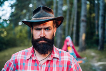 Mature Hipster With Beard. Brutal Man With Beard In Hat. Brutal Brunette Bearded Man In Hat On A Background Of Trees. Handsome Strong Stylish Man With Long Lush Black Beard And Moustache.