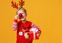 Happy Funny Child Boy In Red Christmas Reindeer Costume With Gift On Yellow   Background.