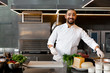 © Andrii - Handsome young African chef standing in professional kitchen in restaurant preparing a meal of meat and cheese vegetables.