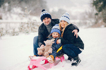  Family have fun in a winter park. Stylish mother in a blue jacket. Little girl on a pink sled. Father with cute daughter