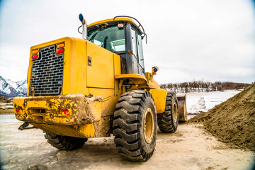 Wall Mural - Focus on a yellow bulldozer with snowy mountain and cloudy sky in the background