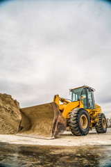 Wall Mural - Front of a yellow bulldozer with mound of soil and cloudy sky in the background