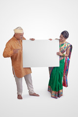 Wall Mural - Couple holding a white blank sign board standing over white background in traditional Indian Kurta Pyjamas and Nauvari Saree.