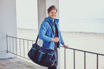 Young attractive trainer with sportive bag is waiting for his command outside.