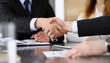 © Iryna - Businessman shaking hands with his colleague or partner above the glass desk in modern office, close-up. Unknown business people at meeting. Teamwork, partnership and handshake concept