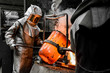 In a foundry workshop. A worker protected by a safety suit pours the molten metal into a mold