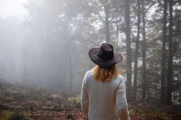 Wall Mural - moody atmosphere in forest. woman wearing knitted sweater and hat standing in fog