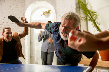 Wall Mural - Young people playing table tennis in workplace, having fun. Friends in casual clothes play ping pong together at sunny day. Concept of leisure activity, sport, friendship, teambuilding, teamwork.