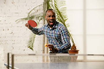 Wall Mural - Young man playing table tennis in workplace, having fun. Model in casual clothes plays ping pong exciting at sunny day. Concept of leisure activity, sport, friendship, teambuilding, teamwork, emotions