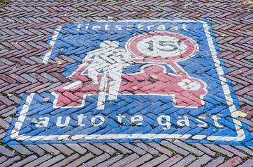 The concept of a Dutch bicycle street in which cars are guests, explained with slightly fading paint on a brick pavement