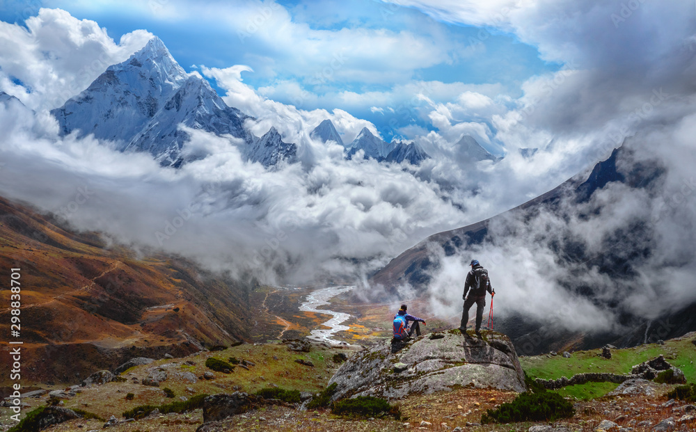 Active hikers hiking, enjoying the view, looking at Himalaya mountains landscape.Tracking to Everest base camp valley with Ama Dablam view. Travel sport lifestyle concept - obrazy, fototapety, plakaty 