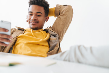 Sticker - Image of african american guy using smartphone and earbuds in office