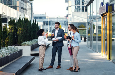 Wall Mural - Group of coworkers having a coffee brake together, standing outside in front of office buildings and talking.