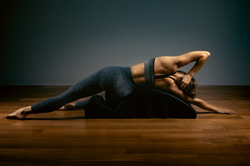 Pilates, fitness, sport, training and people concept - woman doing exercises on a small barrel. Fitness concept, low key, gray background, copy space, art light.