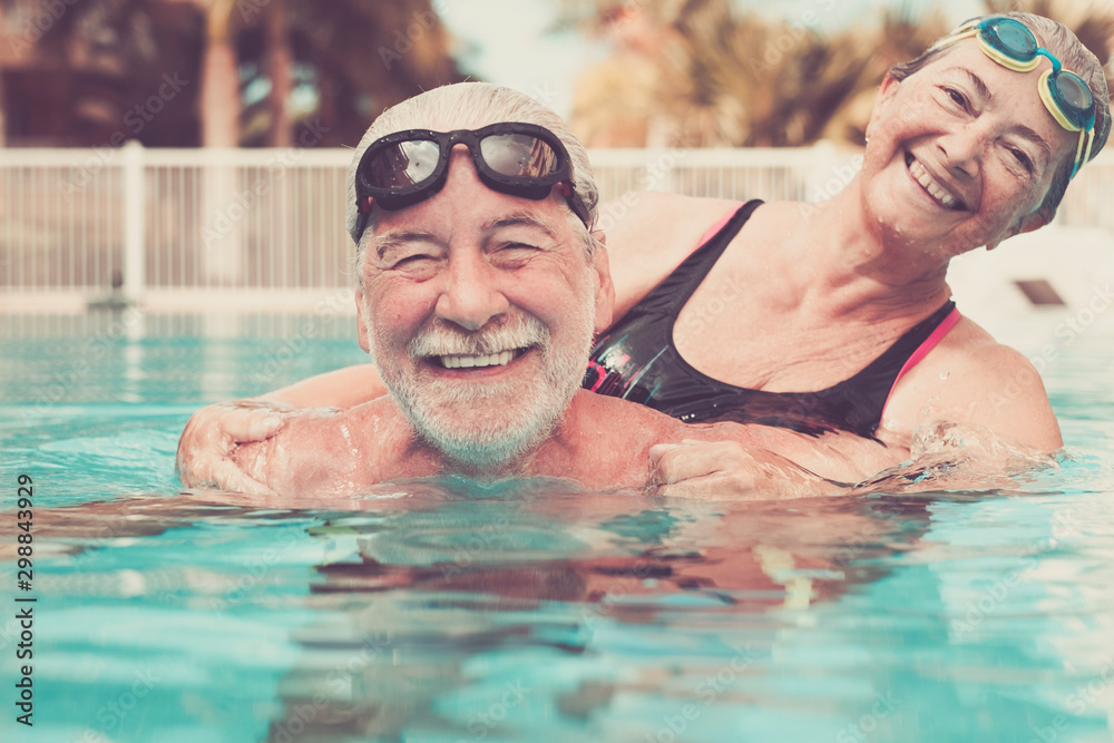 couple of two seniors hugged in the water of swimming pool - active man and woman doing exercise together at the pool - hugged with love - obrazy, fototapety, plakaty 