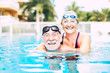 two seniors or mature people together hugged in the blue water of the swimming pool - active woman and man doing exercise together - summertime and having fun