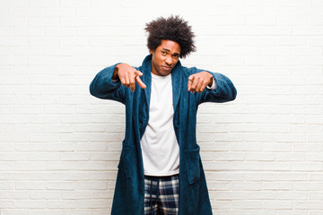 Wall Mural - young black man wearing pajamas with gown pointing forward at camera with both fingers and angry expression, telling you to do your duty against brick wall