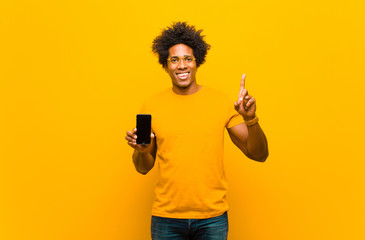 Wall Mural - young african american man with a smart phone against orange bac