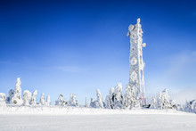 Frozen Television Or Cellular Tower In Heavy Snow Near Ski Center. Telecommunication Towers With Dish And Mobile Antenna Against Blue Sky In Winter Mountains.