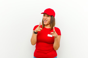 delivery woman smiling with a positive, successful, happy attitude pointing to the camera, making gun sign with hands against white background