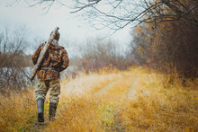Male Hunter Walking On The Road In The Forest In Autumn. The Gun In The Case On The Shoulder Of The Hunter.