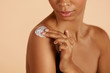 Skin care. Closeup woman's body with cosmetic cream on skin. Beautiful black girl with moisturizing lotion on hydrated body skin at studio