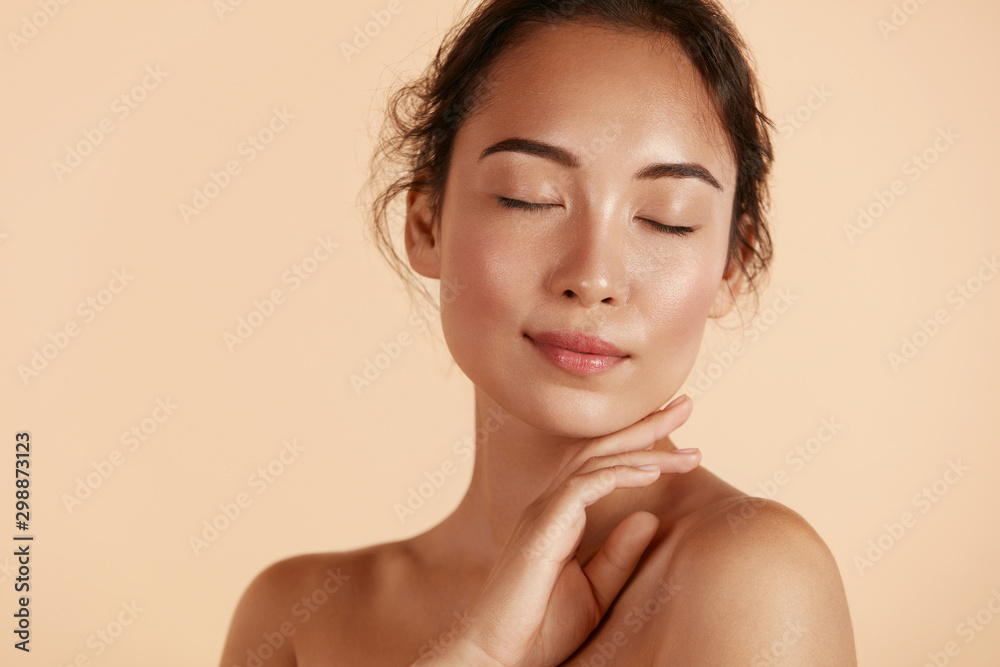 Beauty face. Woman with natural makeup and healthy skin portrait. Beautiful asian girl model touching fresh glowing hydrated facial skin on beige background closeup. Skin care concept - obrazy, fototapety, plakaty 