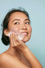Wall Mural - Face skin care. Smiling woman using facial oil blotting paper portrait. Closeup of beautiful happy asian girl model with natural makeup using oil absorbing sheets, beauty product at studio