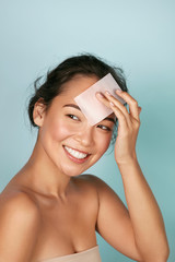 Wall Mural - face skin care. smiling woman using facial oil blotting paper portrait. closeup of beautiful happy a