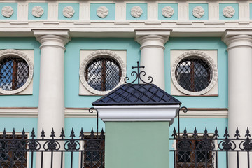 Fragment of the facade of an old building with columns, round windows, and forged fence