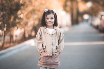 Wall Mural - Smiling kid girl 3-4 year old wearing stylish jacket and skirt posing over city background outdoos. Looking at camera. Childhood. Autumn season.