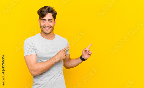 Fotografía smiling happily and pointing to side and upwards with both hands showing object