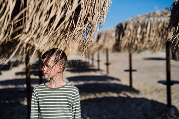 Wall Mural - A small boy standing among straw parasols outdoors on beach.