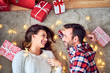 © baranq - Smiling couple relaxing together lying on floor in room filled with Christmas lights and presents