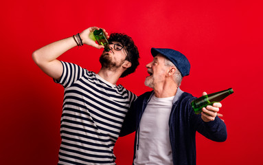 Wall Mural - Young man and senior father with bottles in a studio on red background.