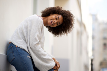 happy young african american woman leaning against wall outside