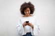 © mimagephotos - smiling young african american woman looking at cellphone by white wall