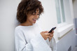 © mimagephotos - Close up happy smiling african american young woman looking at mobile phone outside by white wall