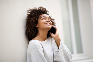 Wall Mural - close up beautiful african american young woman talking with cellphone by white wall